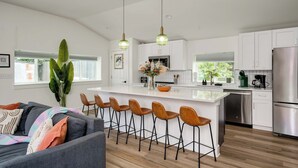 A modern kitchen with white cabinets, a stainless steel refrigerator, and a central island with bar stools. - 3/2, Private hot tub, fireplace, firepit (Blanco)