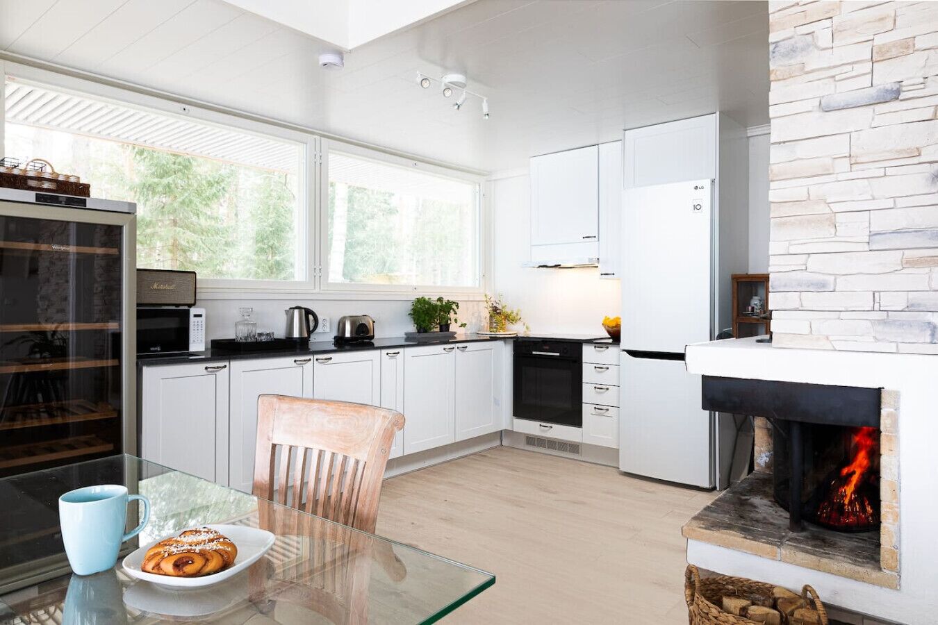 A modern kitchen with white cabinetry, a glass dining table, and a fireplace.