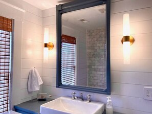 A bathroom with a large mirror, white tiles, a sink with two faucets, and a towel hanging on the wall.