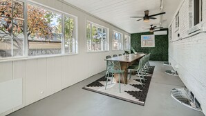 A dining area with a wooden table and chairs, large windows, and ceiling fans.