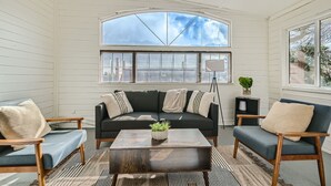 A cozy room with a dark green sofa, two armchairs, a wooden coffee table, and a large arched window.