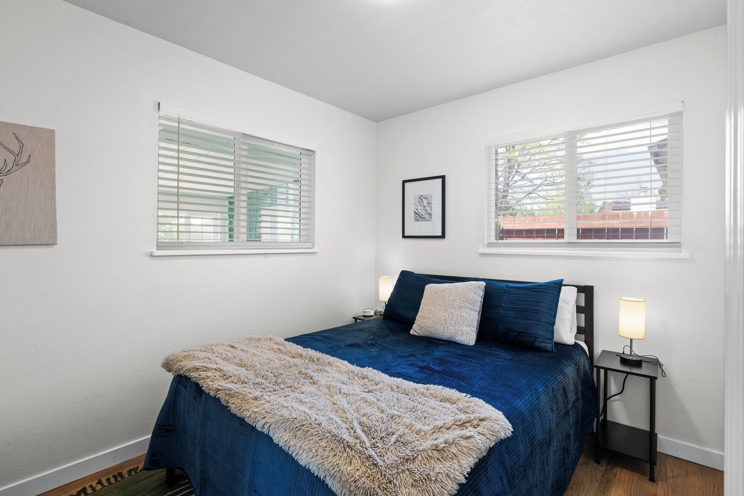 A bedroom with a large bed, two bedside tables with lamps, and a window with blinds.