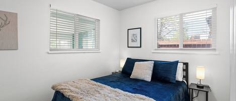 A bedroom with a large bed, two bedside tables with lamps, and a window with blinds.