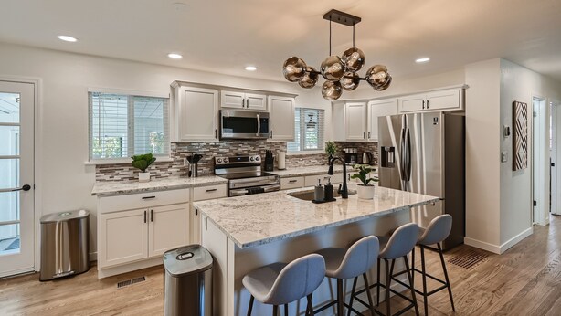 A modern kitchen with white cabinets, stainless steel appliances, a central island with bar stools, and a decorative ceiling light.