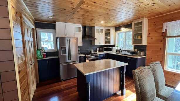 A modern kitchen with wooden ceiling, stainless steel appliances, and a central island.