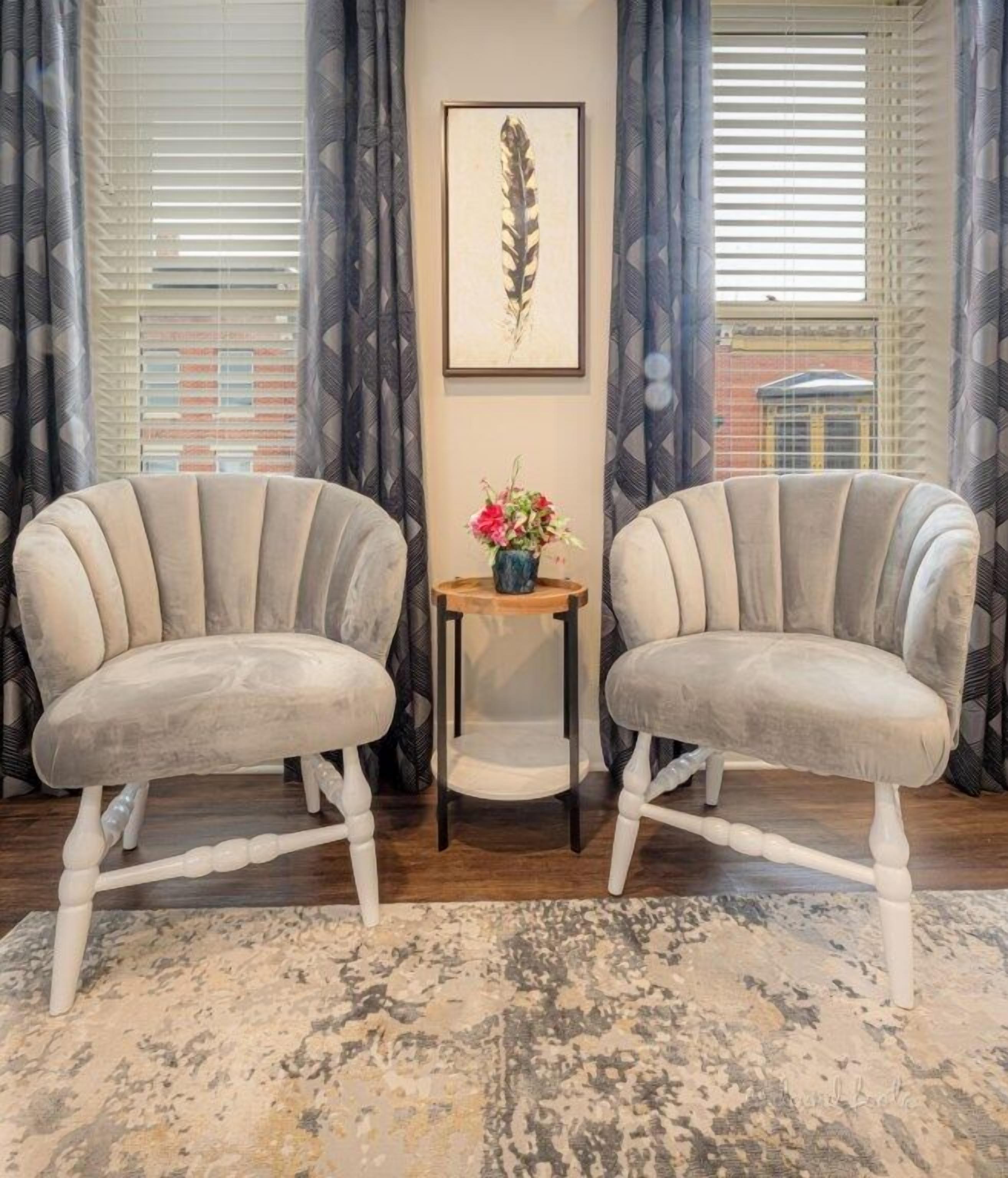 Two upholstered chairs with wooden legs and a small wooden table with a vase of flowers between them.