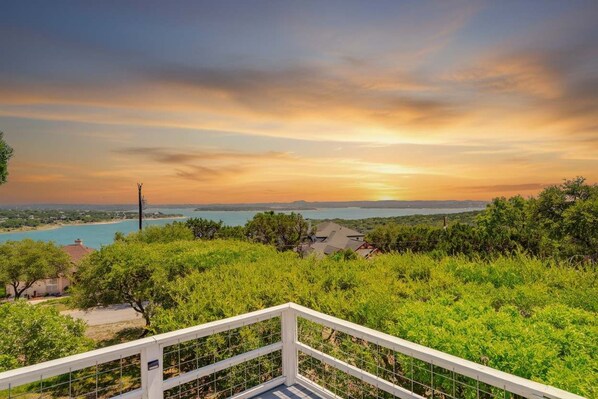A scenic view of a coastal landscape with a sunset, a body of water, and a white fence in the foreground.