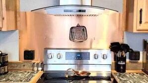 Une cuisine équipée d’une cuisinière en acier inoxydable, d’une hotte aspirante et de meubles de rangement en bois.