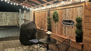 Une terrasse extérieure dotée d’un espace salon couvert, d’un mur en bois sur lequel est accroché un panneau indiquant « fait maison », et de guirlandes lumineuses.