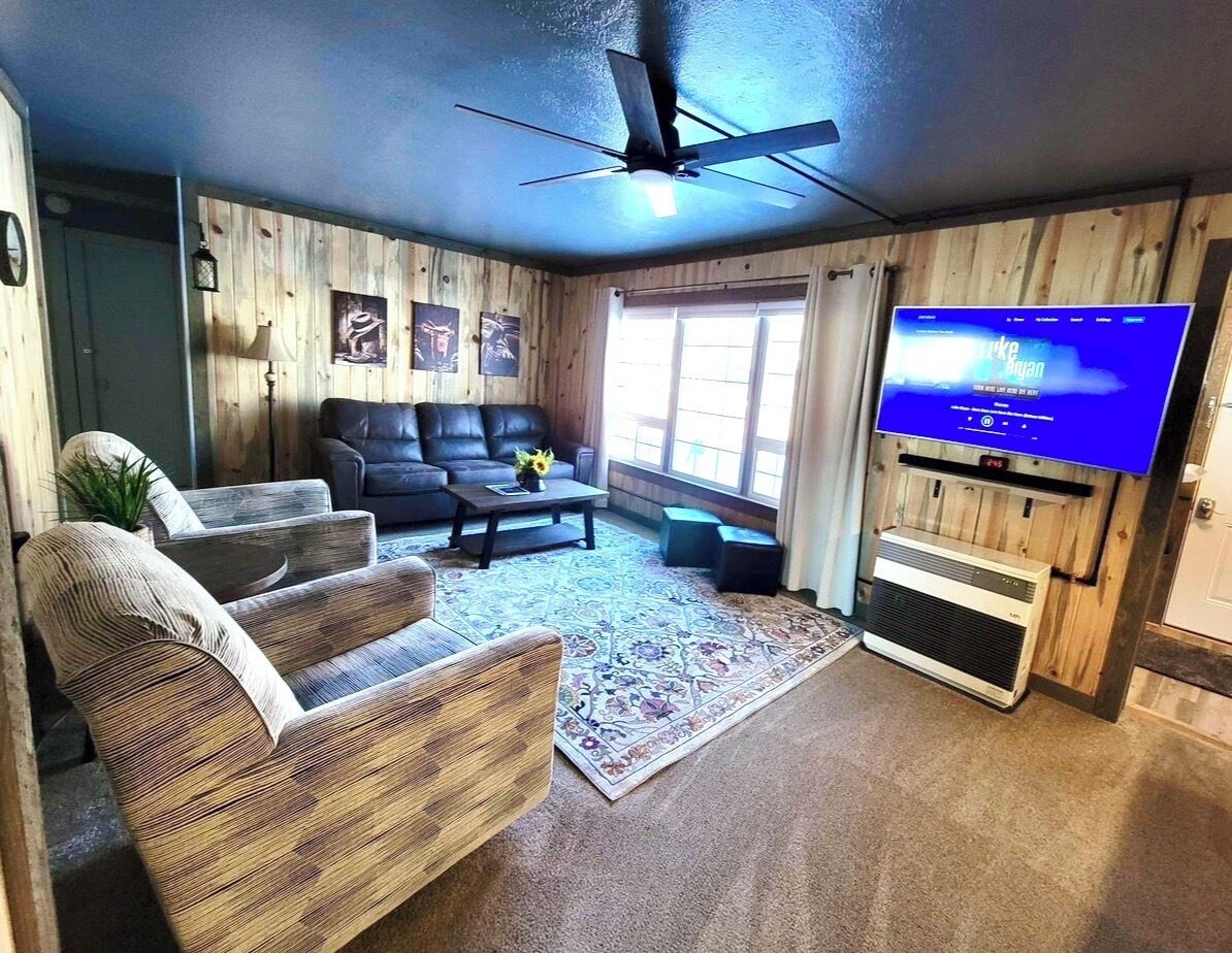 Un salon doté d’un ventilateur de plafond, d’un téléviseur à écran plat, d’une cheminée et d’une grande fenêtre.