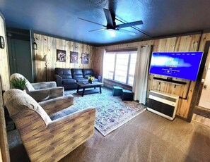 A living room with a ceiling fan, a flat-screen TV, a fireplace, and a large window. - Single Story Home in a quiet neighborhood (Lakeview)