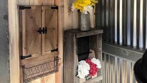 Un mur rustique agrémenté d’une armoire en bois, d’une horloge et d’étagères ornées de fleurs.