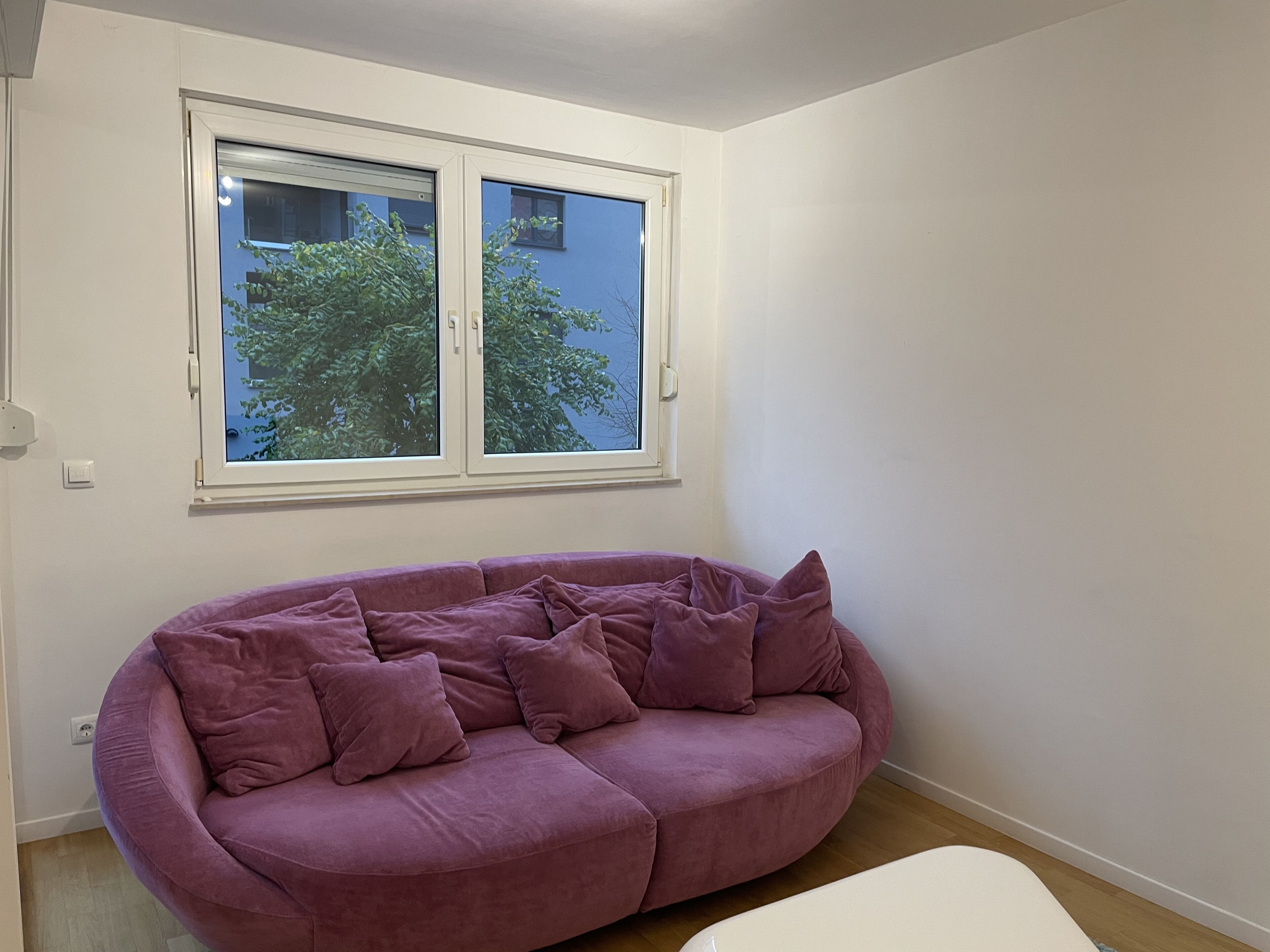 A room with a purple sofa, a white bench, and a window with a view of trees.