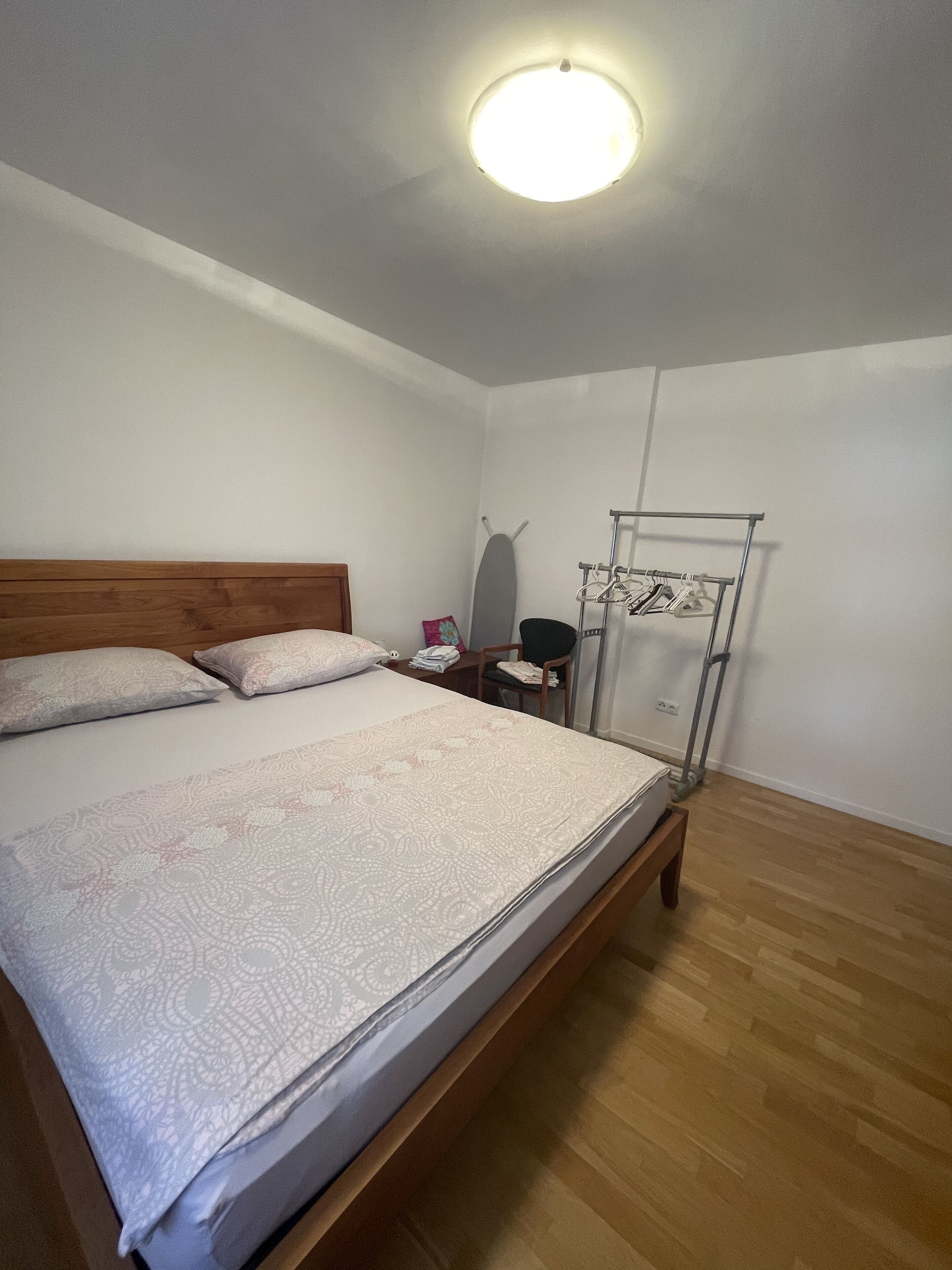 A bedroom with a bed, a nightstand, a wall-mounted ironing board, and a drying rack.