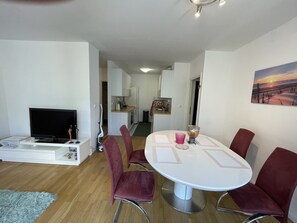 A modern living room with a TV, a dining table with chairs, a kitchen in the background, and a painting on the wall. - Large Modern 75m2 Flat and Free Parking (Zagreb)