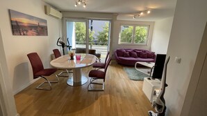 Una sala de estar moderna con una mesa de comedor redonda, sillas rojas, un sofá púrpura y un mueble para el televisor.