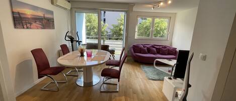 A modern living room with a round dining table, red chairs, a purple sofa, and a TV stand.