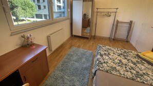 Un dormitorio con un ventanal grande, un radiador, un armario, un espejo y una cama con edredón estampado.