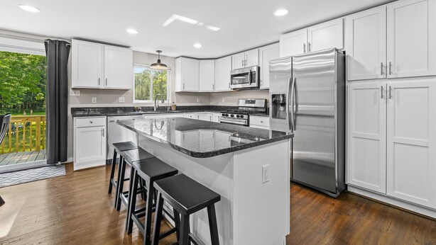 A modern kitchen with white cabinets, stainless steel appliances, and a central island with bar stools. - Higgins Hideout *3 minute drive to the beach* (Roscommon)