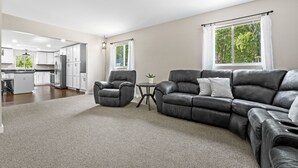 A spacious living area with a modern kitchen in the background, a leather sofa, and a small round table with a plant. - Higgins Hideout *3 minute drive to the beach* (Roscommon)
