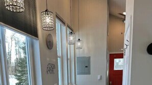 Un espacio habitable compacto con kitchenette, una zona de comedor con taburetes de bar, un sofá con cojines y una puerta roja.