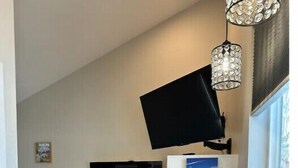 Habitación pequeña con cama, escritorio, silla, televisor en la pared y ventana.