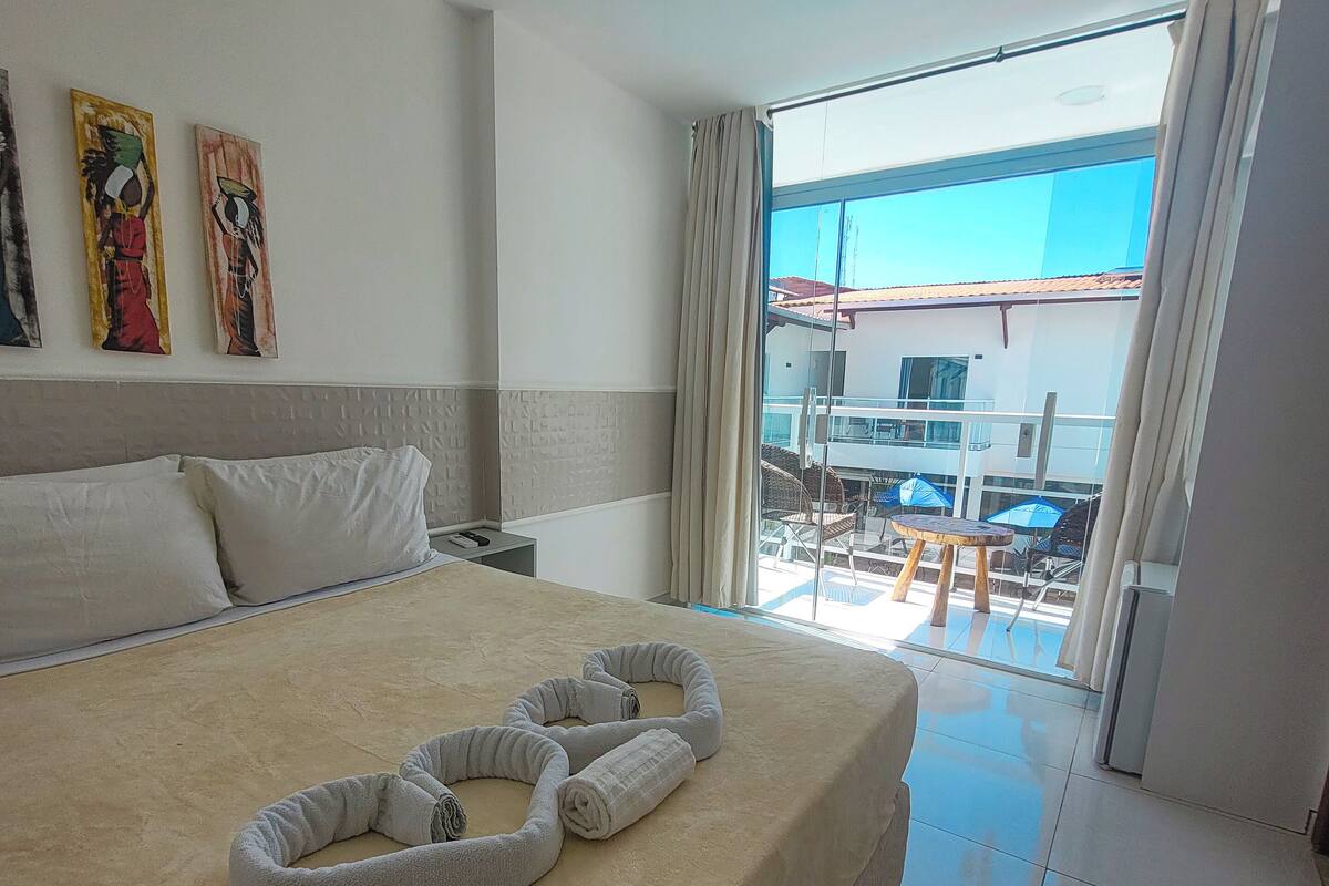 Hotelkamer met een groot bed, een balkon met een tafel en stoelen, en kunst aan de muur.