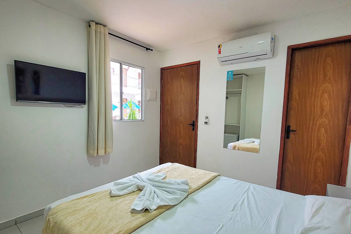 Een hotelkamer met een bed, een televisie, een airconditioner en een raam met gordijnen.