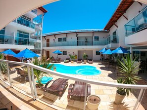 Un espace piscine aménagé sur le toit, avec des chaises longues et des parasols, entouré de plantes en pot et bordé d’un immeuble à plusieurs étages doté de balcons.