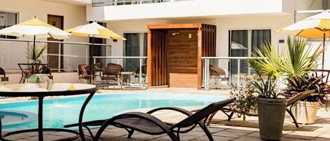 A pool area with lounge chairs, umbrellas, and potted plants.