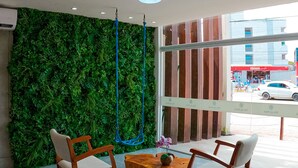 Un interior moderno con una pared verde, dos sillas de madera, una mesita redonda y una hamaca azul colgante.