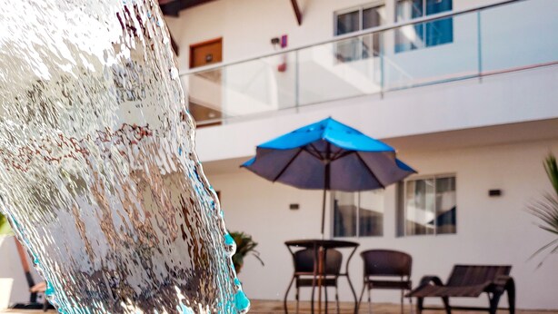 Una piscina con fuente de agua cristalina, una sombrilla azul y mobiliario exterior.