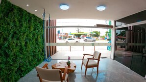 Un interior moderno con una pared verde, dos sillas de madera, una mesa redonda pequeña y vista a la calle.
