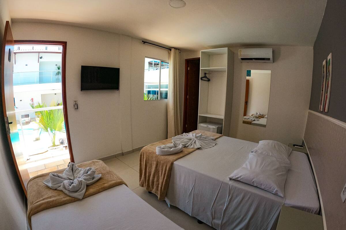 Een hotelkamer met twee bedden, een televisie, een kledingkast, een spiegel en een balkon met uitzicht op een zwembad en groen.