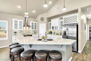 A spacious kitchen with a large island, stainless steel appliances, and bar stools. - Spacious gulf view home on north beach with enclosed yard & balconies (Corpus Christi)