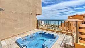 Ein Whirlpool auf einem Balkon mit Blick auf das Meer und ein Gebäude im Hintergrund.