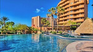 Ein Hotel mit Pool, Palmen und einem Gebäude mit Strohdach.