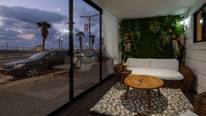 A modern interior with a large window, a white sofa, a wooden table, and a green wall with hanging plants. - Tripel-A (Tel Aviv)