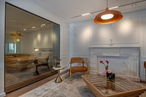 Ein modernes Wohnzimmer mit einer großen Glasswand, einem Kamin, einem Holzstuhl, einem Couchtisch und einer hängenden Deckenleuchte.