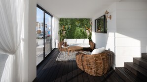 A modern balcony with a wicker sofa, a small round table, and a green wall with plants. - Tripel-A (Tel Aviv)