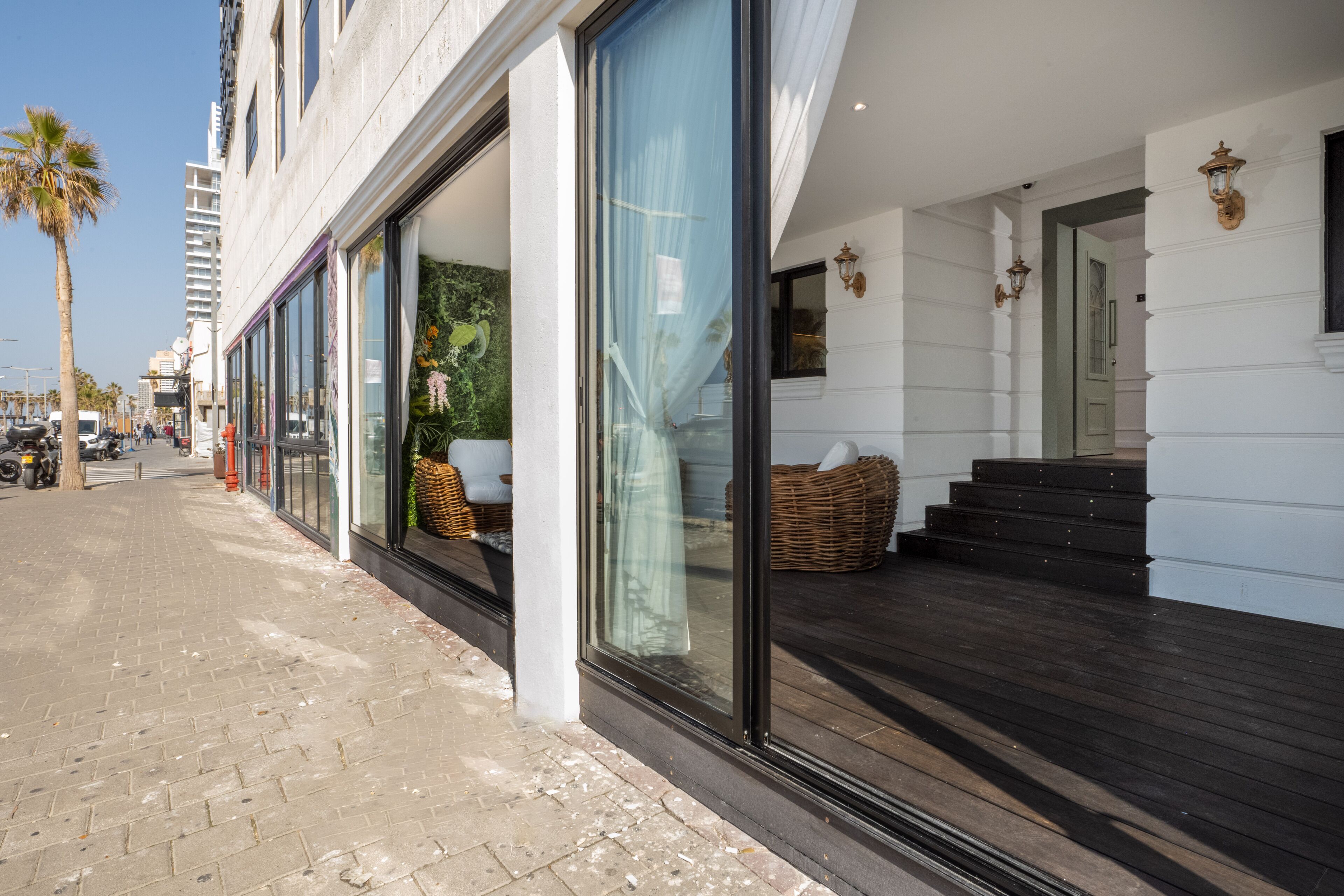 A hotel with large glass windows, a wooden deck, and wicker furniture.