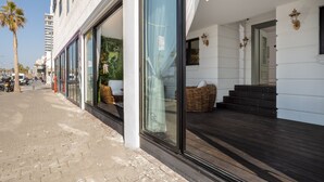 A hotel with large glass windows, a wooden deck, and wicker furniture. - Tripel-A (Tel Aviv)