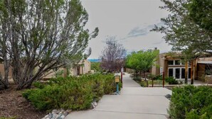 A pathway leading to a building with a covered entrance, surrounded by greenery and trees.