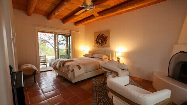 A bedroom with a large bed, a sofa, a fireplace, and a view of the outdoors.