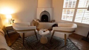 A cozy living room with a fireplace, two armchairs, a small round table, and a patterned rug.