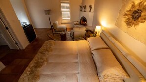 A cozy bedroom with a large bed, a fireplace, and a wall-mounted artwork. - Peaceful Suite in Desert Inn- Acoma Queen Room (Ojo Caliente)