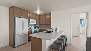 A modern kitchen with a refrigerator, microwave, and island with bar stools. - Belmont Patio - Ocean View, Pet Friendly, Patio, & Garage (San Diego)