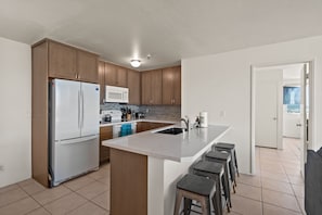 Uma cozinha moderna com frigorífico, micro-ondas e ilha com banquetas.