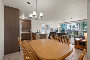 A spacious kitchen with wooden cabinets, a dining table, and chairs. There is a large window with a view of palm trees. - Belmont Patio - Ocean View, Pet Friendly, Patio, & Garage (San Diego)