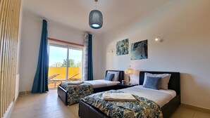 A hotel room with two beds, a balcony, a ceiling light, and artwork on the walls.